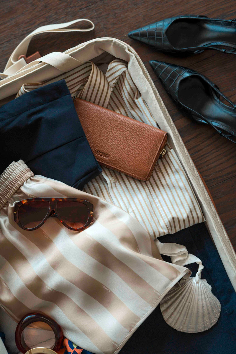 Open Bric's Bellagio suitcase packed with clothes, a leather wallet and sunglasses
