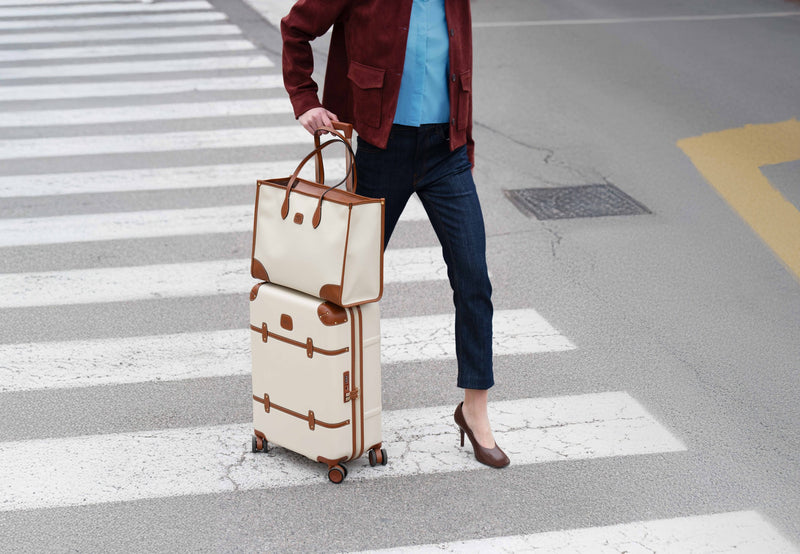 Traveler crossing the street pulling a cream Bric's Bellagio spinner with a matching bag on top