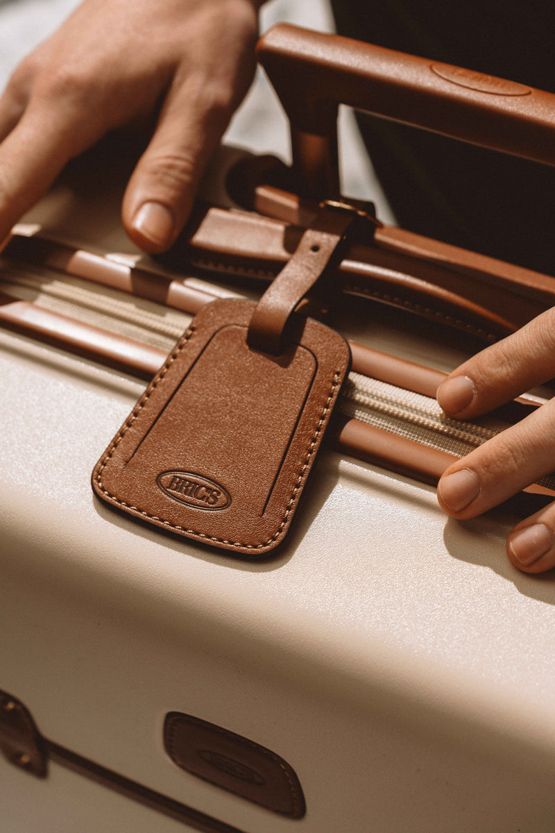 Hands on the leather handle and leather luggage tag of a Bric's Bellagio suitcase
