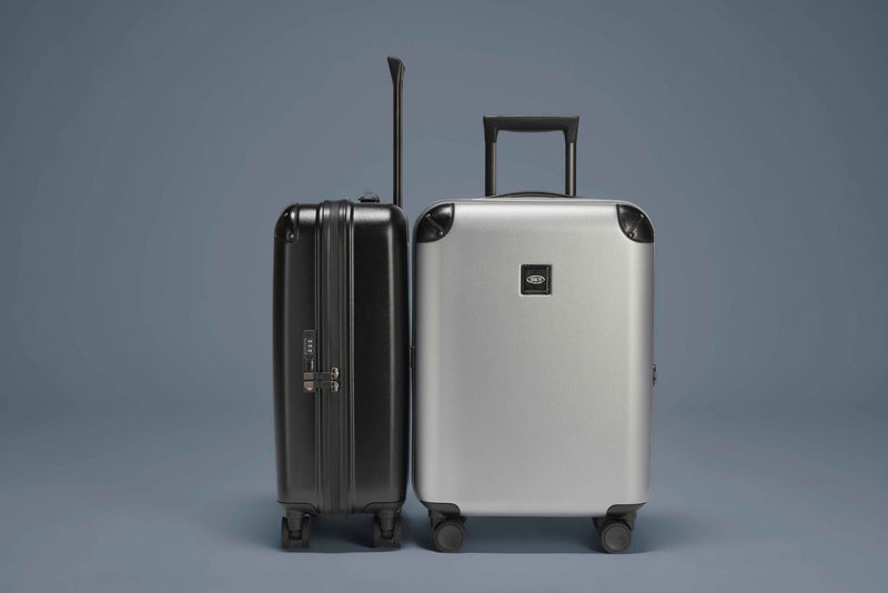 Black and silver Bric's Amalfi 21" carry-on spinners standing side by side on a gray backdrop