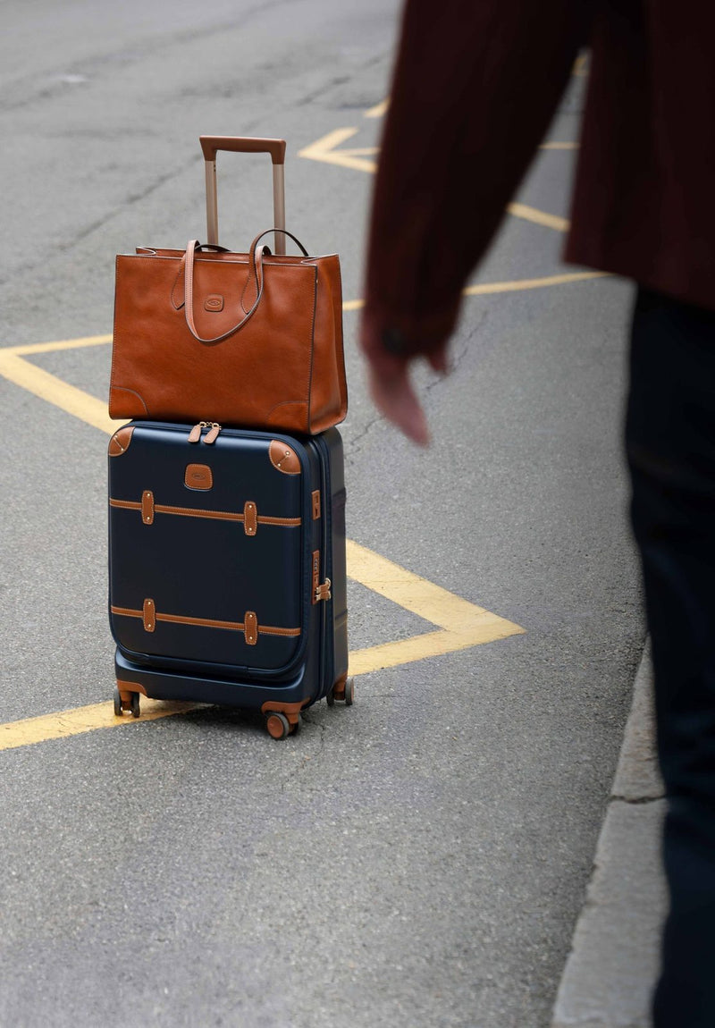 Blue Bric's Bellagio carry-on spinner on a street with a tan leather bag resting on top
