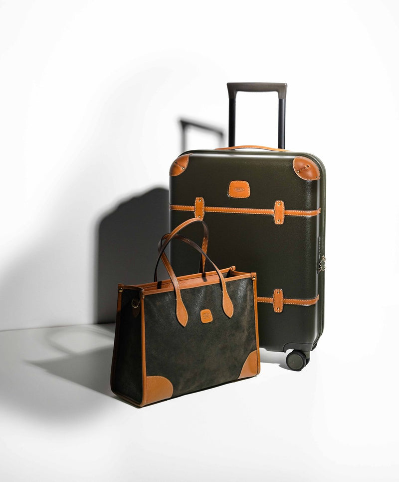 Olive Bric's Bellagio carry-on spinner with its handle raised beside a leather-trimmed tote