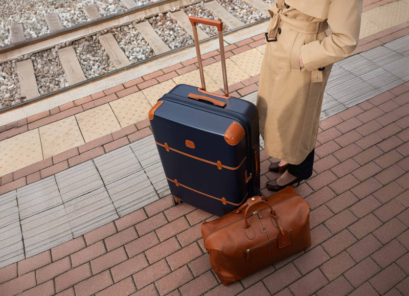 Traveler on a station platform with a blue Bric's Bellagio checked spinner and a tan duffle