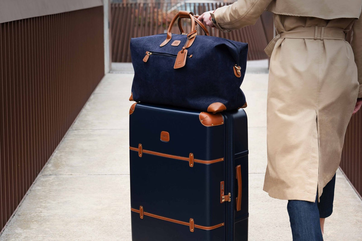 Traveler rolling a blue Bric's Bellagio checked spinner with a matching blue bag resting on top