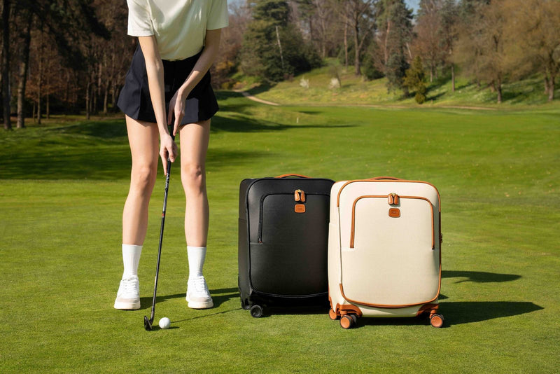 Black and cream Bric's Firenze carry-on spinners standing on a golf green beside a player