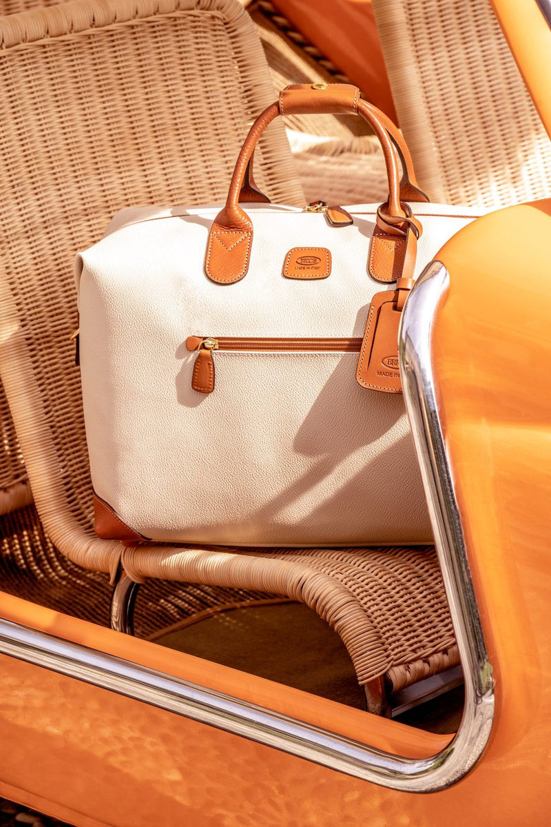 Cream Bric's Firenze Cargo duffle resting on a wicker seat inside an orange vintage car