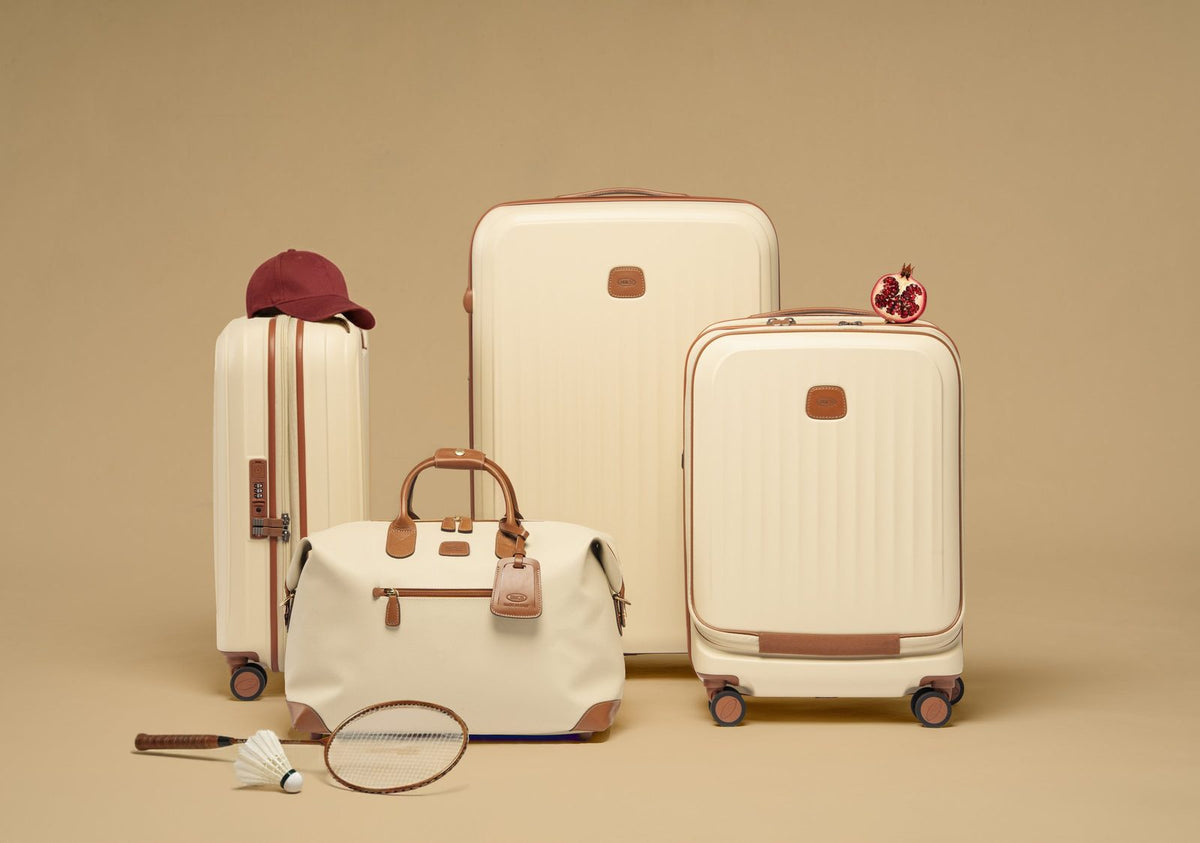 Cream Bric's Firenze Cargo duffle in front of cream Bric's suitcases on a beige backdrop