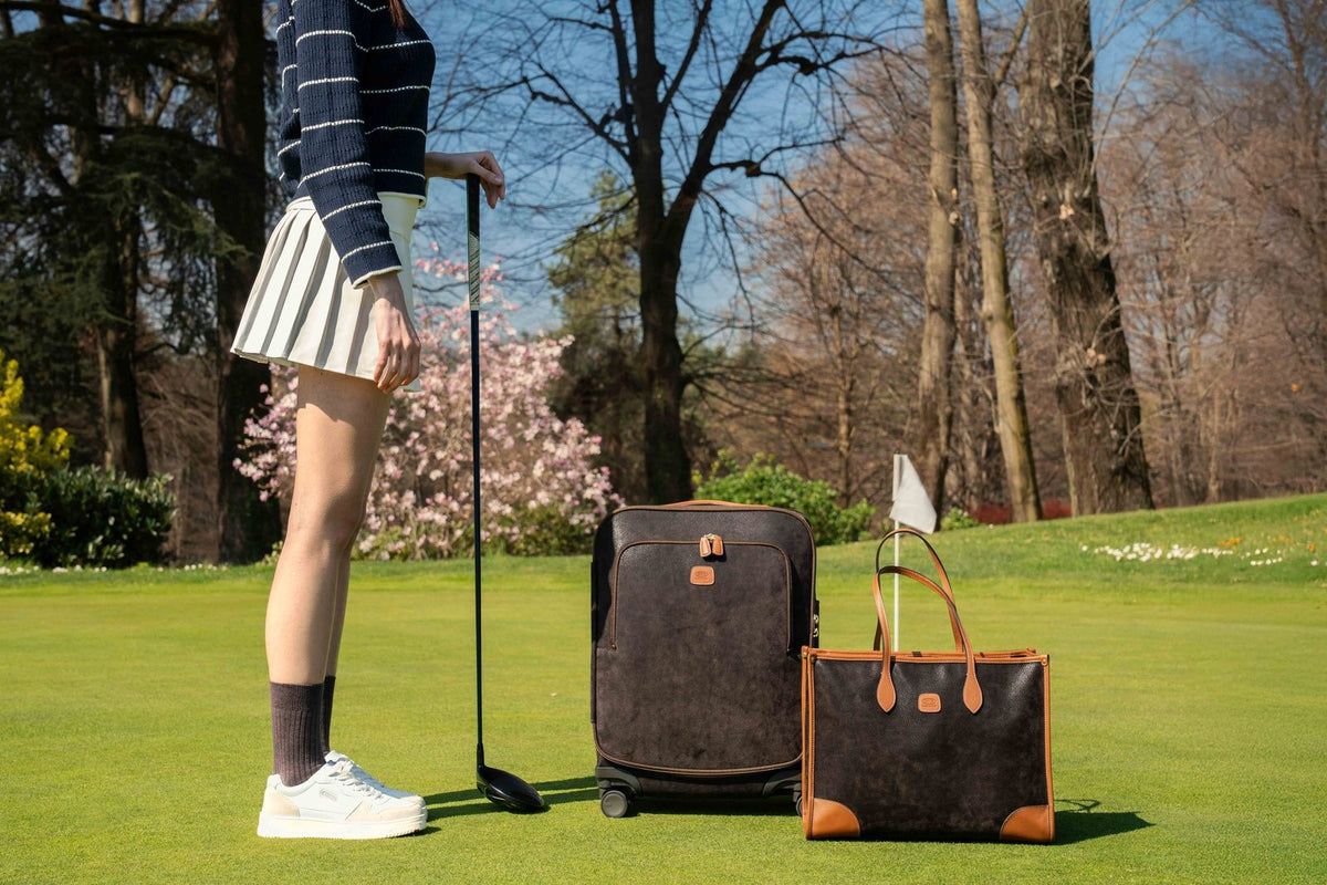 Bric's Life laptop tote beside a spinner suitcase on a golf green, next to a golfer