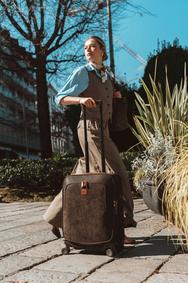 Woman wheeling an olive Bric's Life Compound carry-on along a stone sidewalk