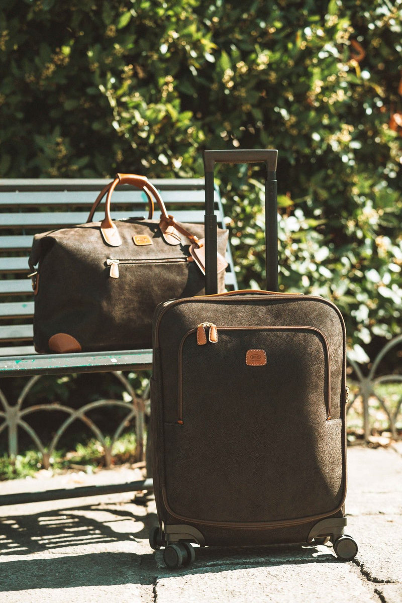 Olive Bric's Life cargo duffle on a park bench beside a suede-effect spinner