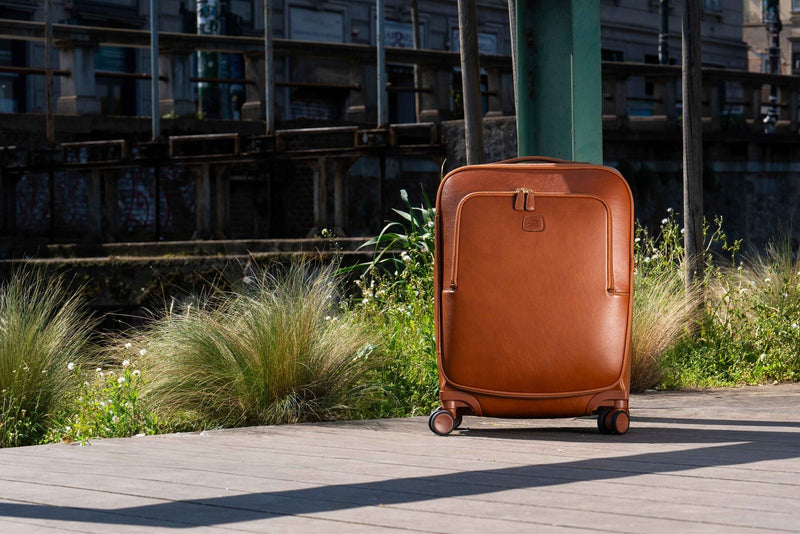 Cognac leather Bric's Life Pelle carry-on spinner standing on a boardwalk beside tall grasses