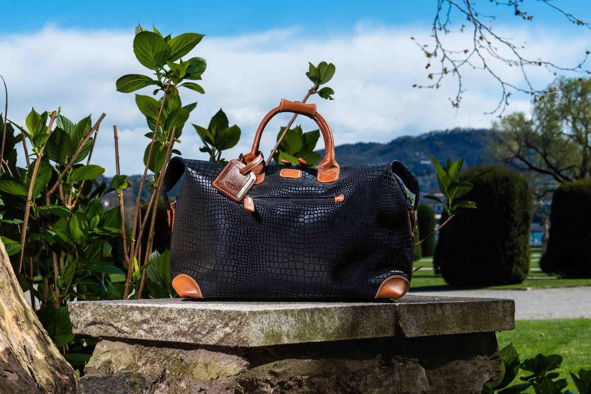 Black Bric's My Safari cargo duffle with tan leather handles on a stone ledge in a garden