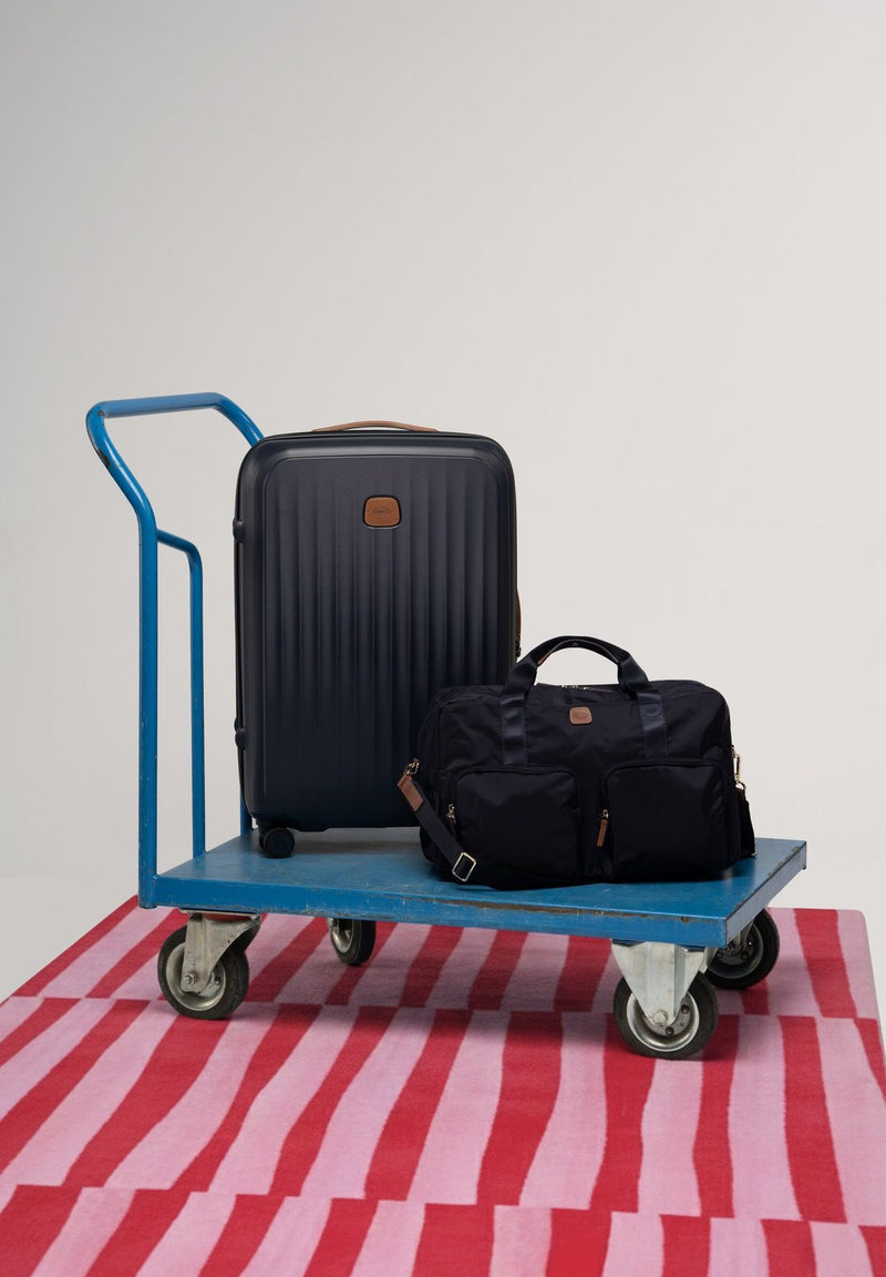Blue Bric's Taormina carry-on spinner and a bag on a blue platform trolley over a striped rug