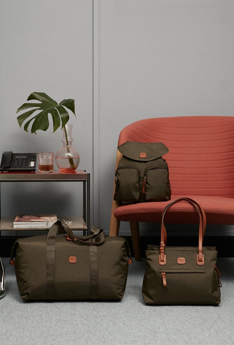 Olive Bric's X-Collection Piccolo backpack on a red chair, with olive X-Collection bags on the floor