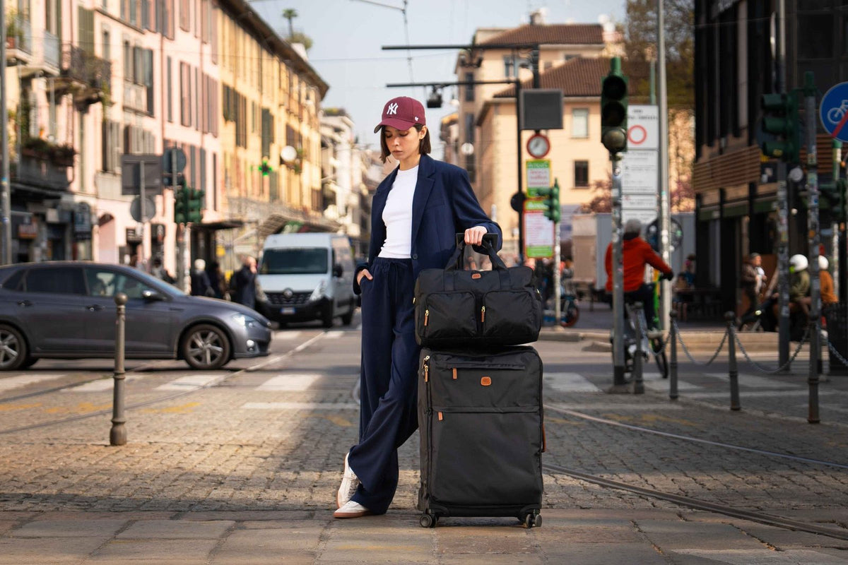 Traveler on a city street with a black Bric's X-Collection boarding duffle on top of a black spinner