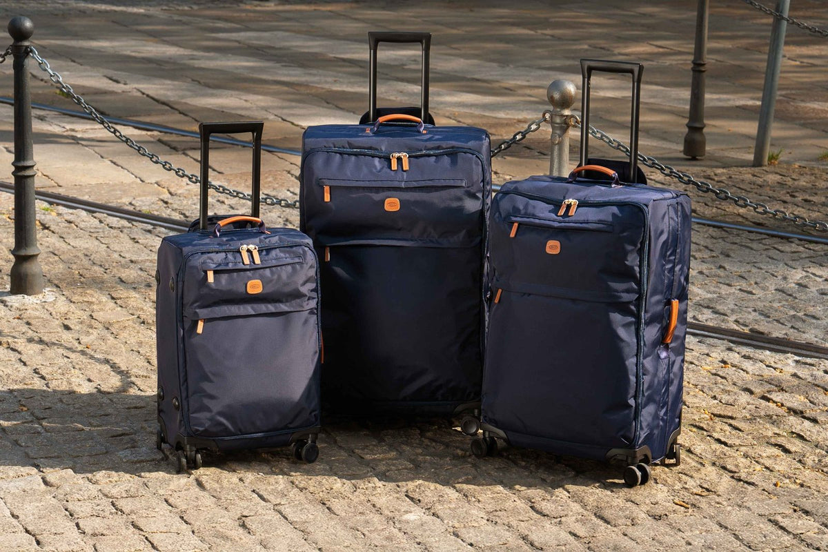 Three navy Bric's X-Collection soft-side spinners in different sizes standing on a cobbled street